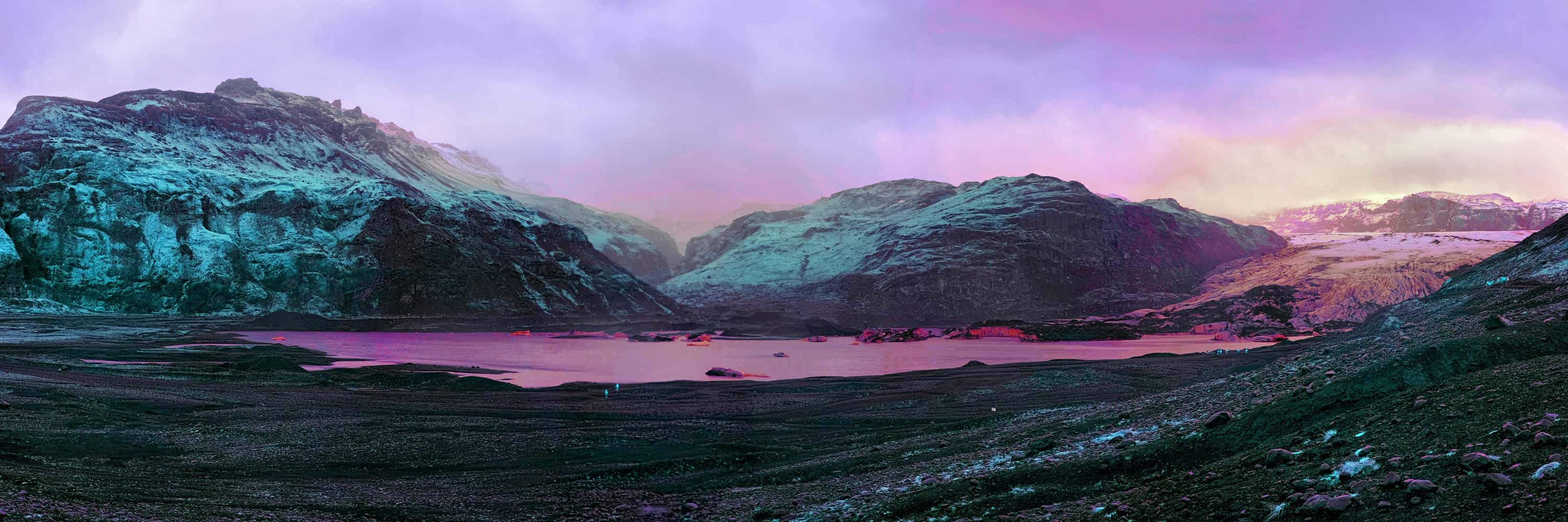 An outlet glacier ending in a small lagoon with floating ice, seen across a moraine plain, photographed in near-infrared light.