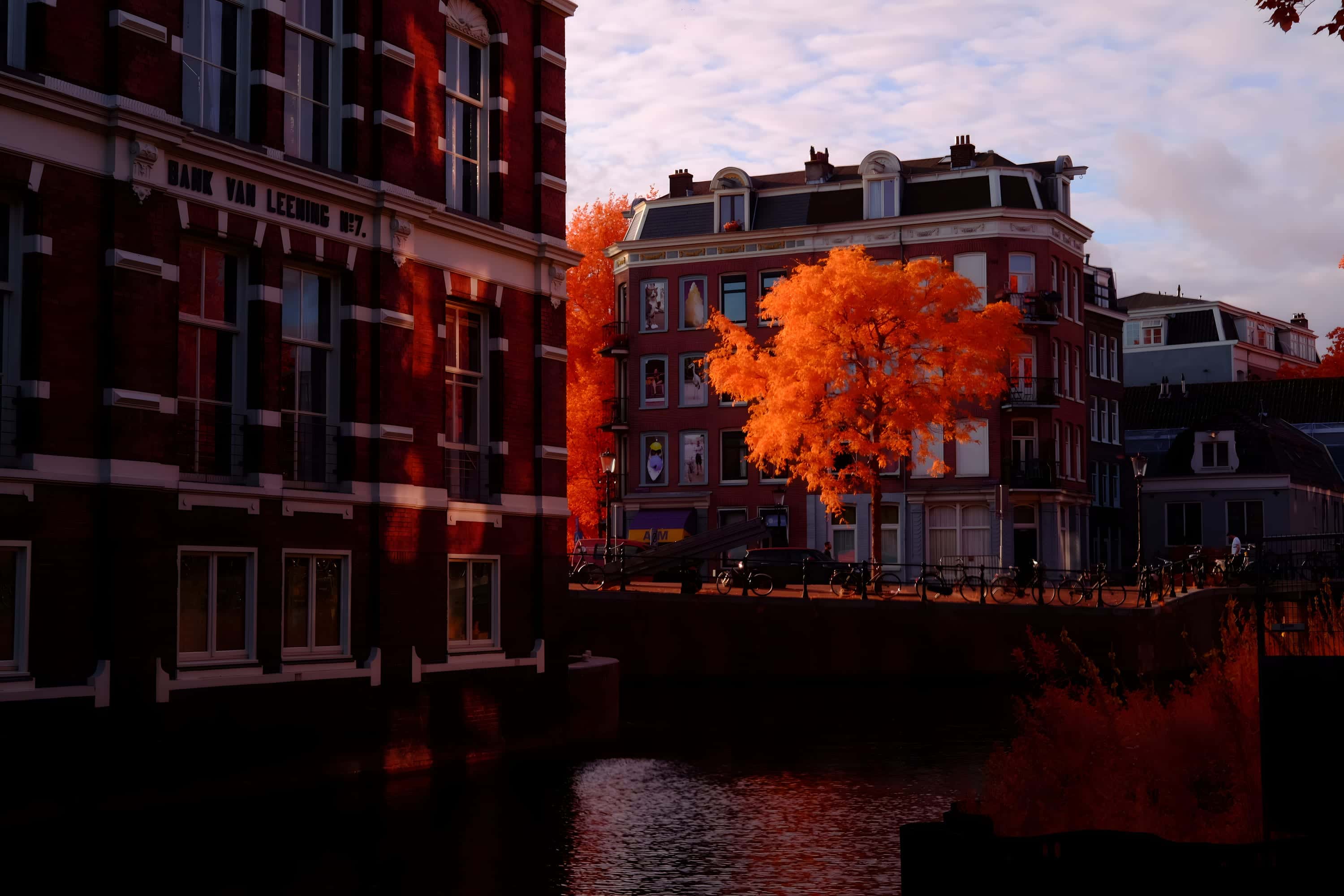 A canal at low sun beside a building inscribed BANK VAN LEENING No. 7, photographed in near-infrared light.