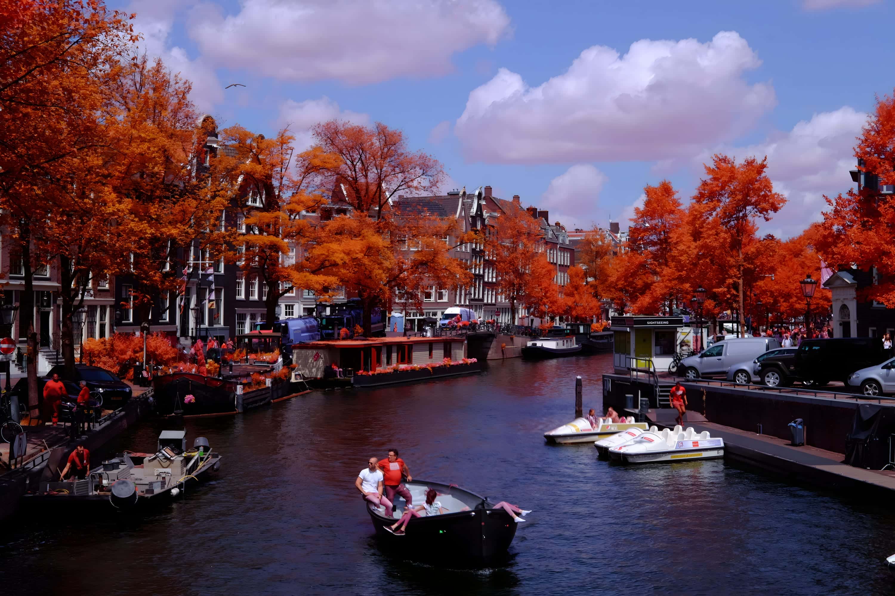 Sightseeing boats, pedal boats and houseboats on an Amsterdam canal seen from a bridge, photographed in near-infrared light.