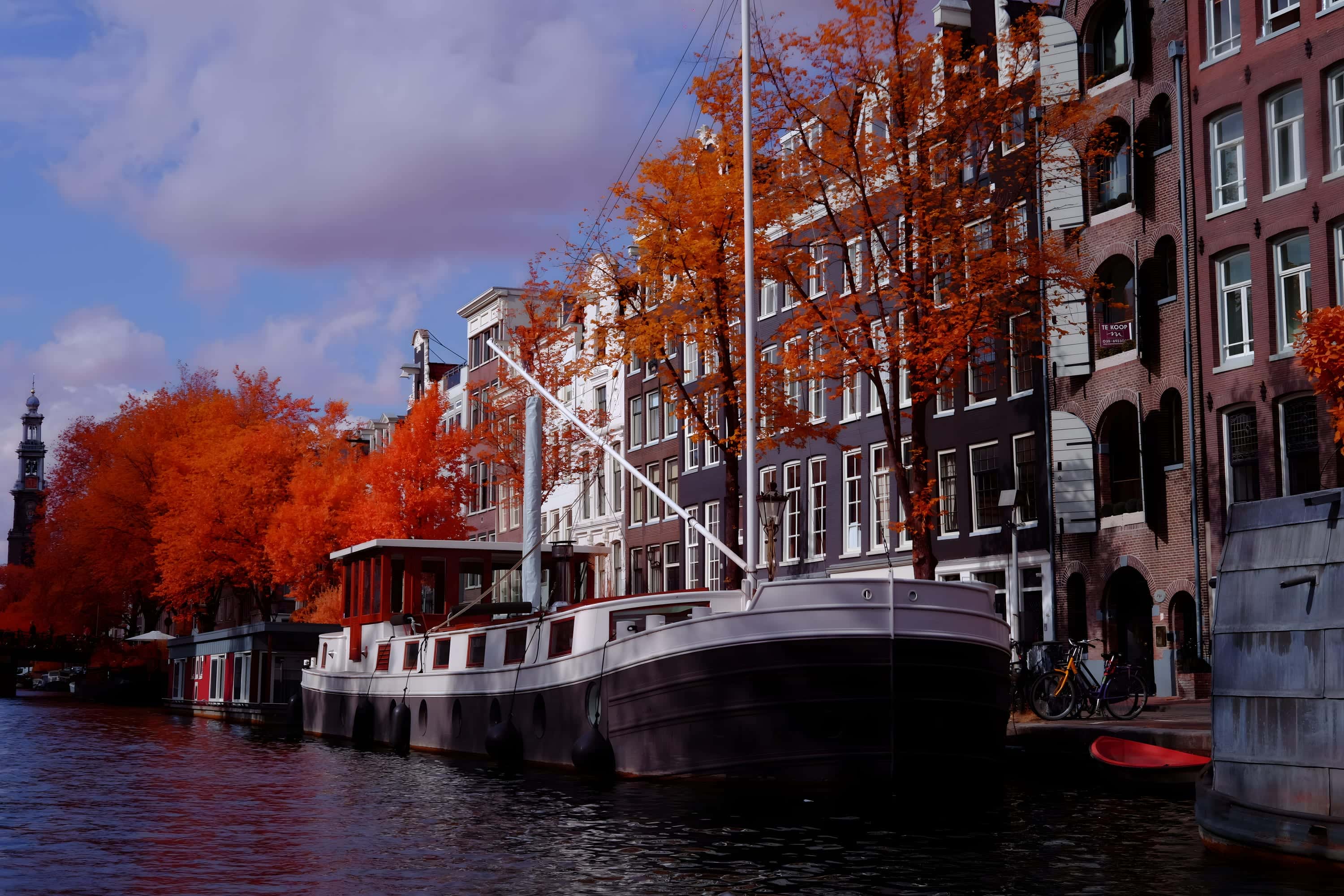A steel barge moored on an Amsterdam canal with the Westertoren visible in the distance, photographed in near-infrared light.